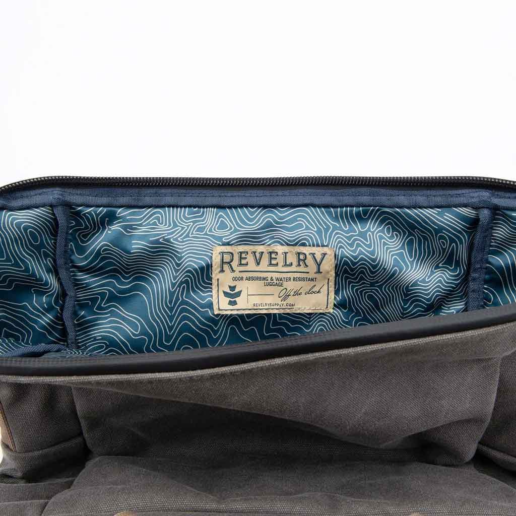 The rolltop closure of the Revelry Supply Drifter backpack displayed open, showing the interior space and organizational pockets.